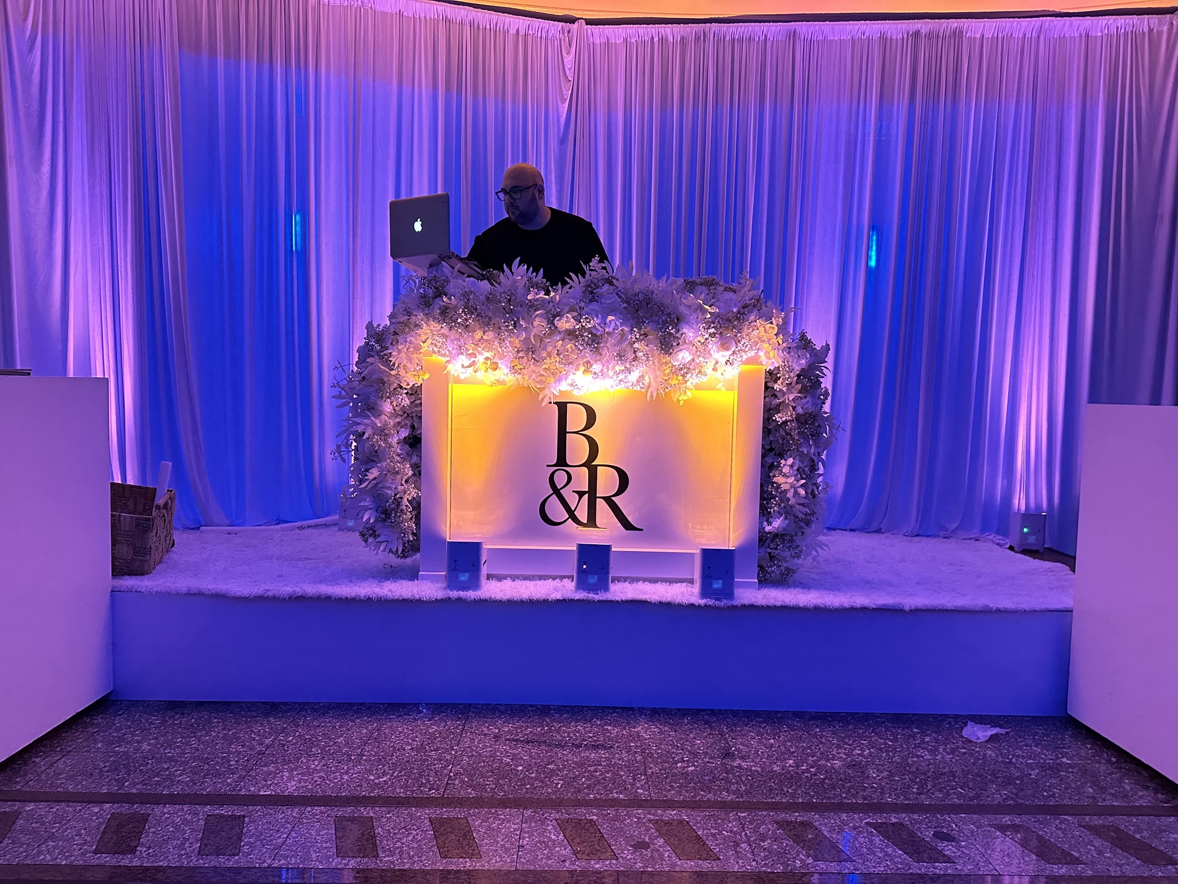 Floral custom DJ booth with monogram and purple uplighting at Sand Castle