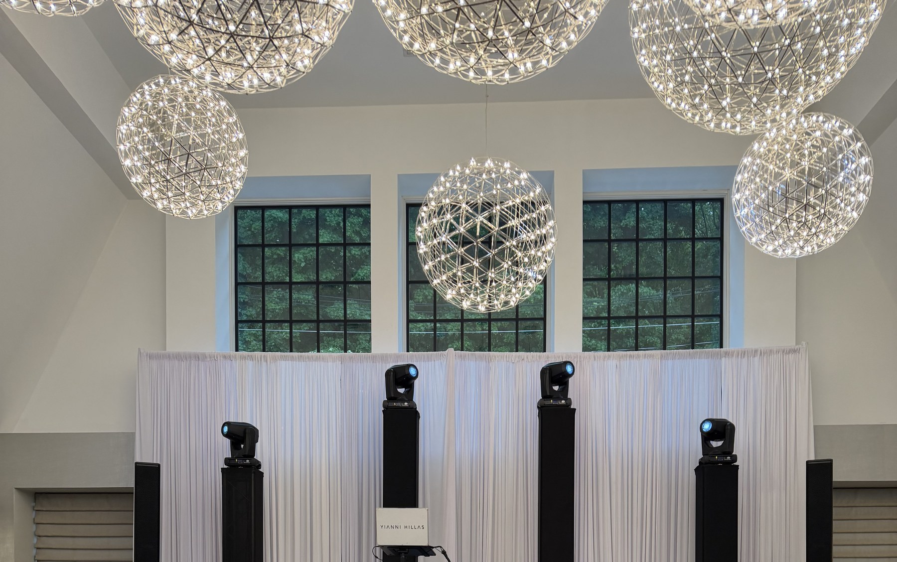 Globe chandeliers and tall windows above the white draped stage at Water's Edge, Centerport